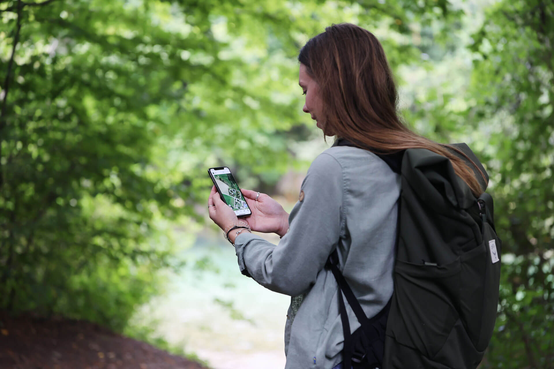 metsässä retkeilevä nainen katselee tractive gps -sovellusta älypuhelimella