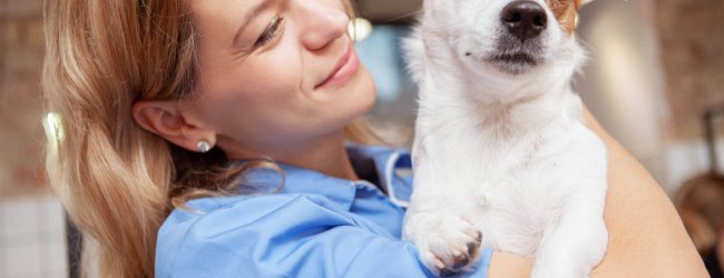 femme tenant un petit chien blanc et brun dans les bras, tourné vers le photographe