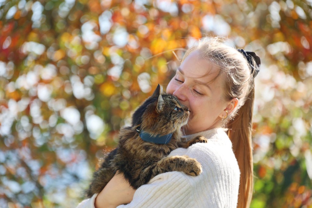 Mujer cogiendo sobre su hombro a un gato marrón con un localizador GPS para gatos en el collar.