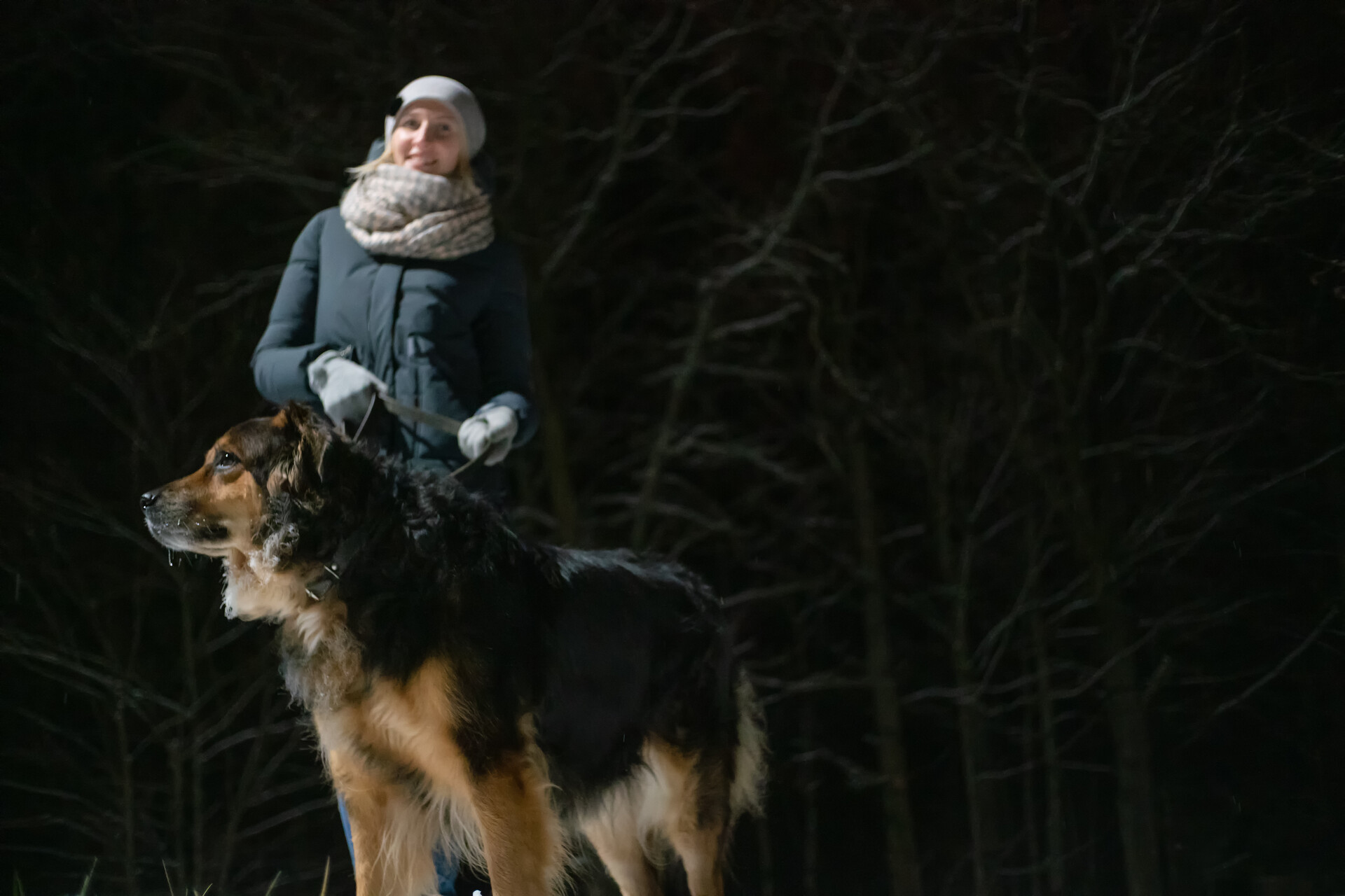 A woman walking her dog on a leash on a dark evening