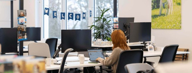 woman working at computer in office with a welcome banner in the background