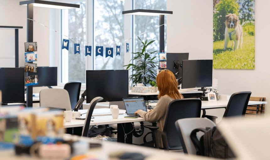 woman working at computer in office with a welcome banner in the background