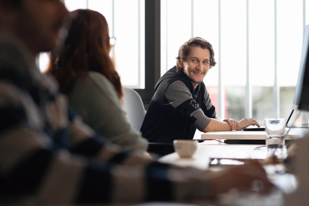 man sitting at desk working, smiling at colleagues