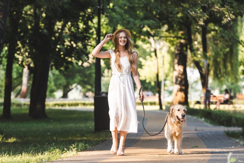 jeune femme en robe blanche avec un chien qui marche à la laisse et porte un gps tractive dans un parc