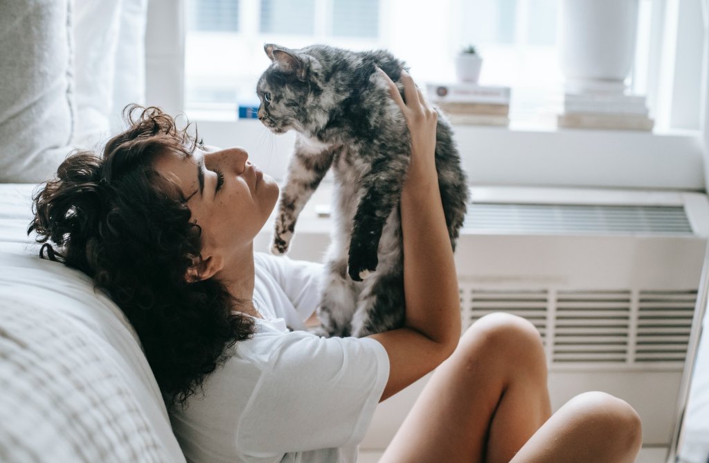 A woman cuddling with her cat besides a bed