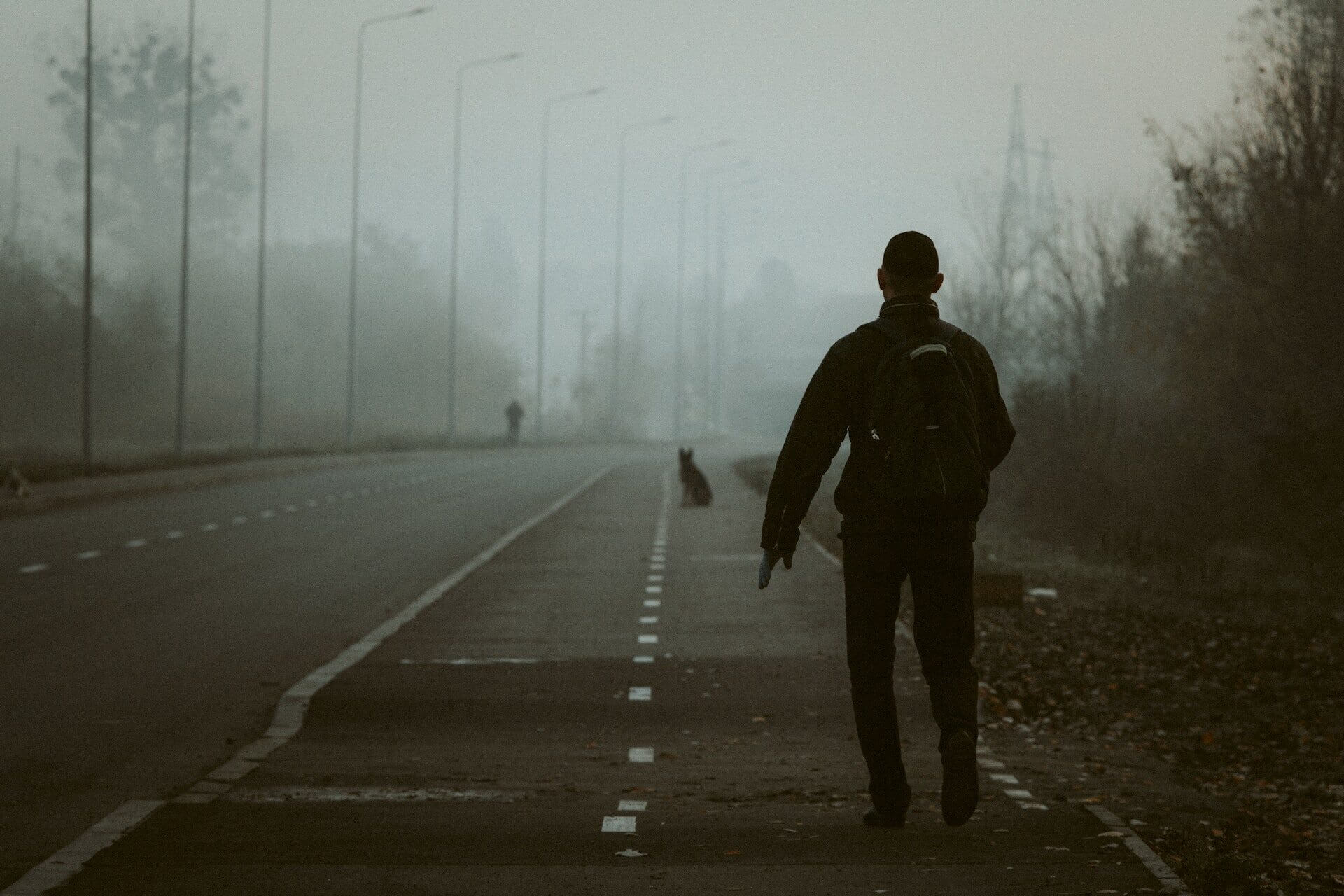 A man chasing a dog that's run away down a street