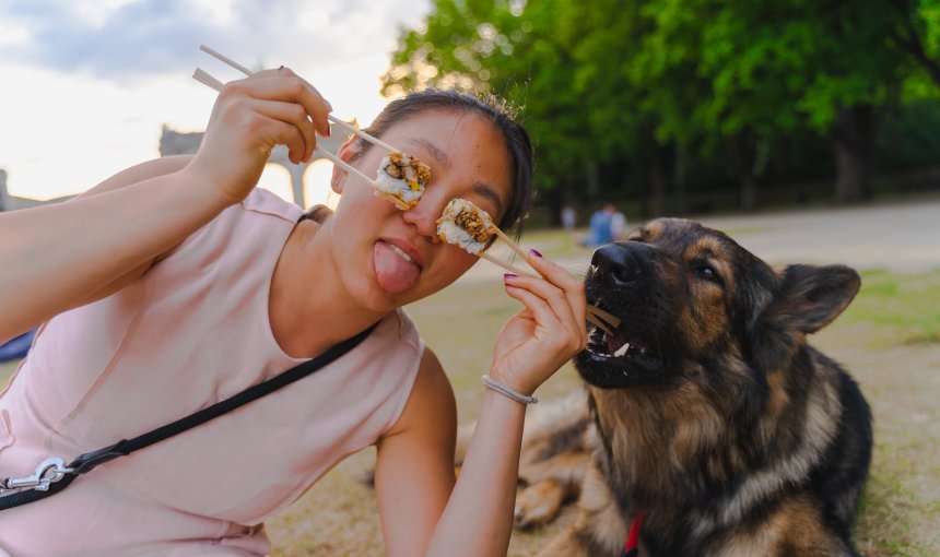 A woman posing with sushi on chopsticks next to her dog