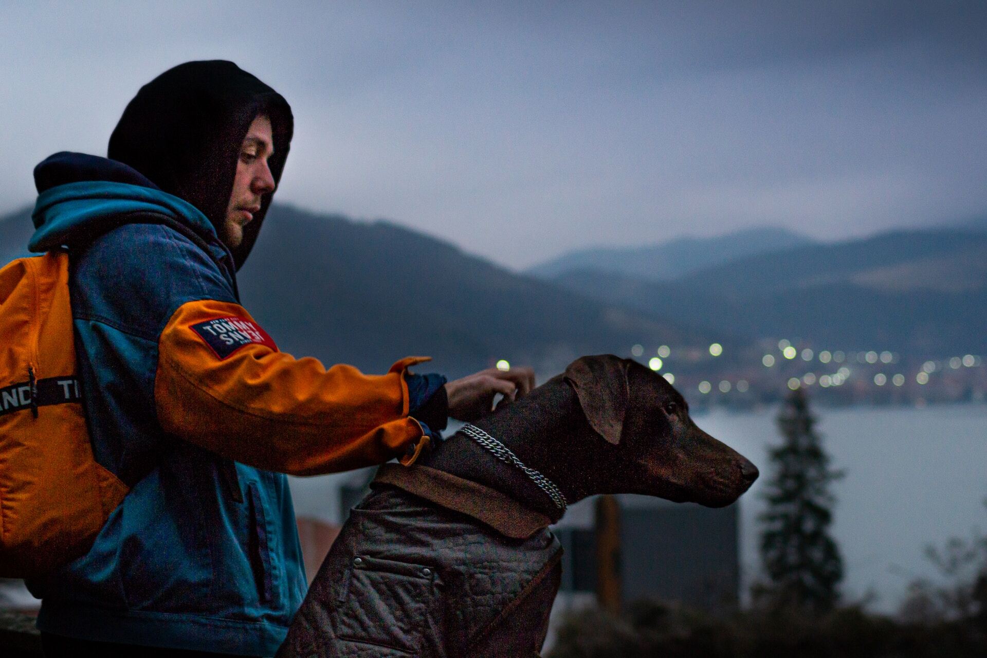 A man walking his dog outdoors on a dark evening