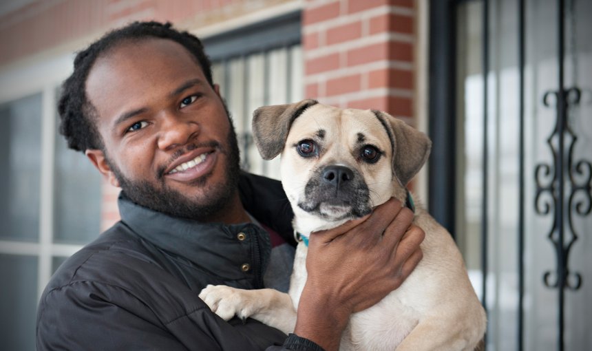 dog owner holds his dog in front of brick house