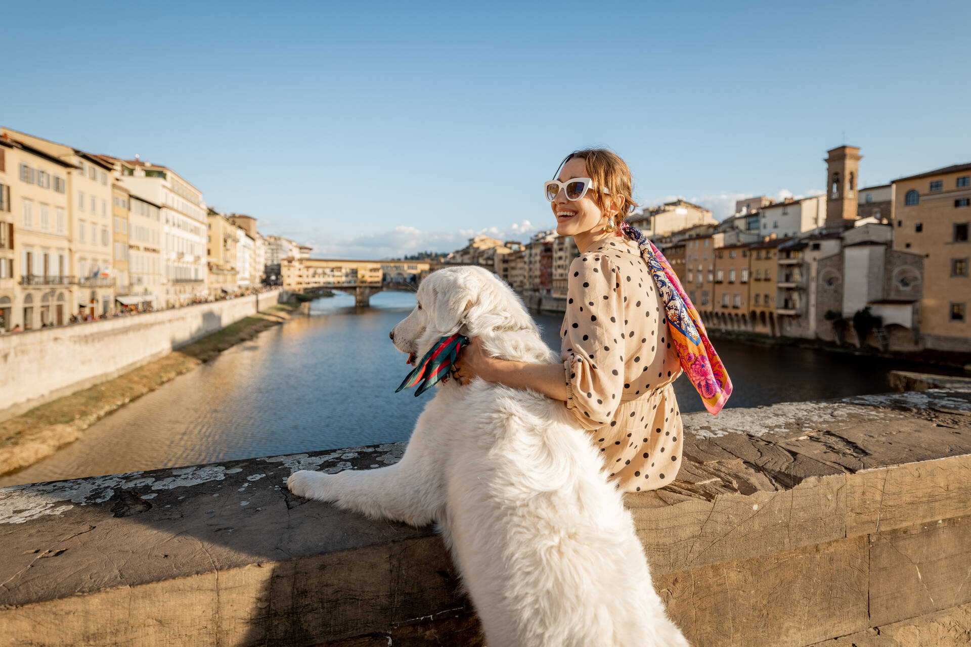 A woman sitting by a bridge with a dog