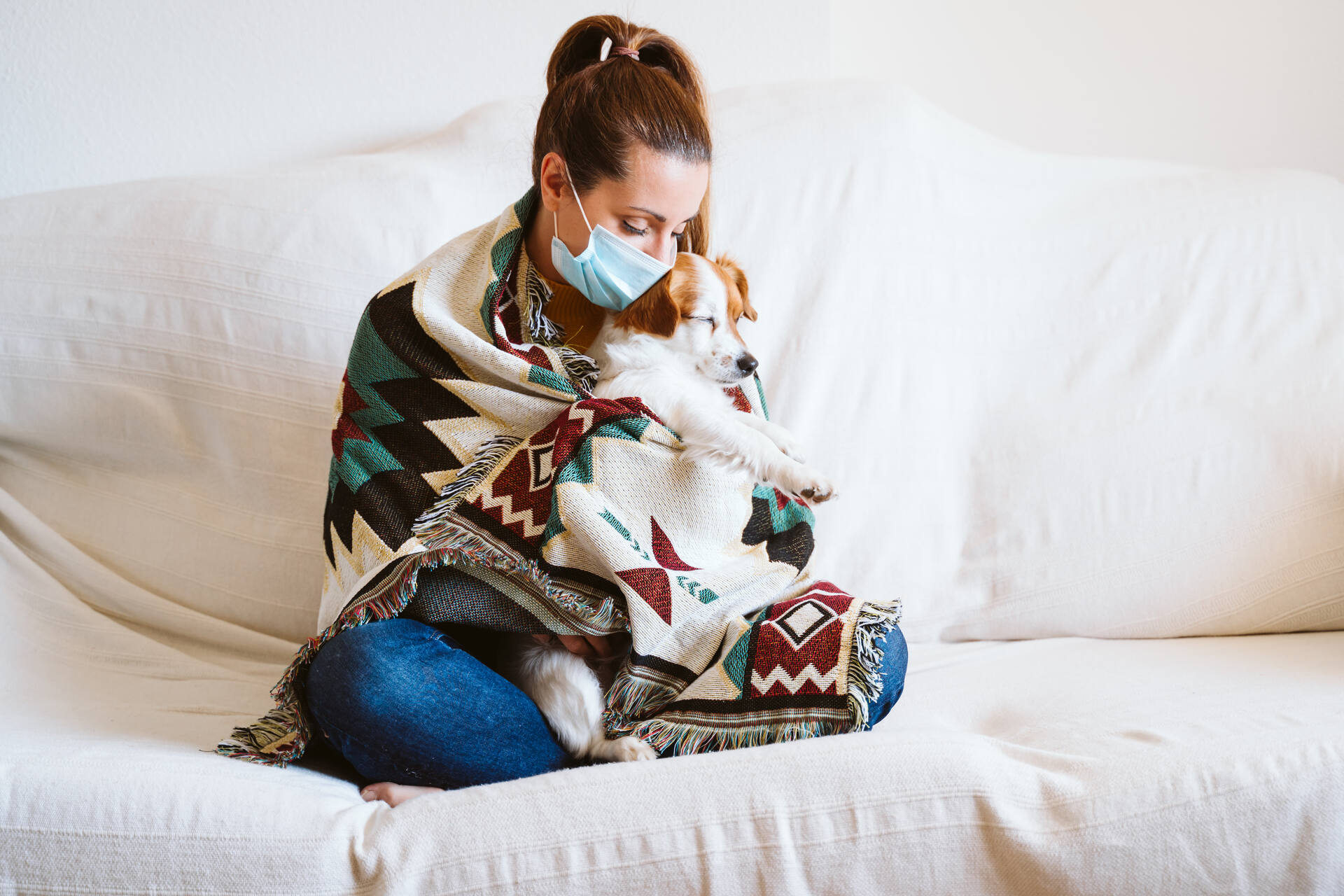 A young woman wearing a mask comforting a sick puppy at home