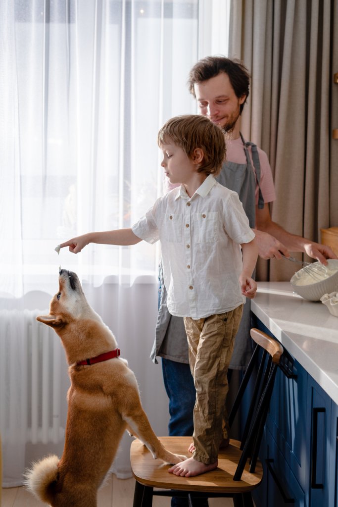 A child distracting a dog while a man cooks