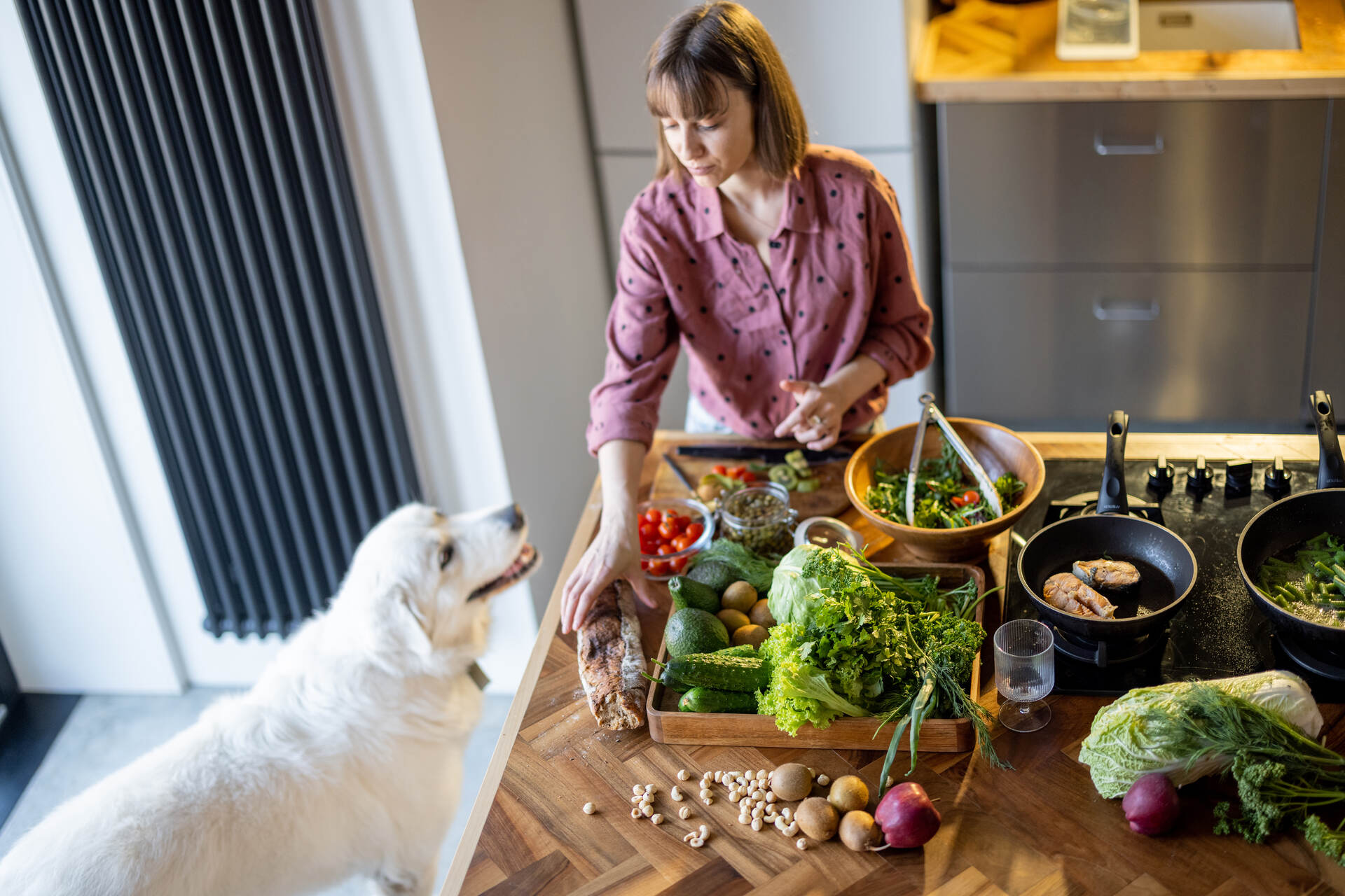 A woman cooking vegetables in the kitchen with her dog