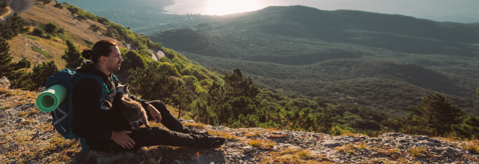 A man hiking with a cat by a mountainside