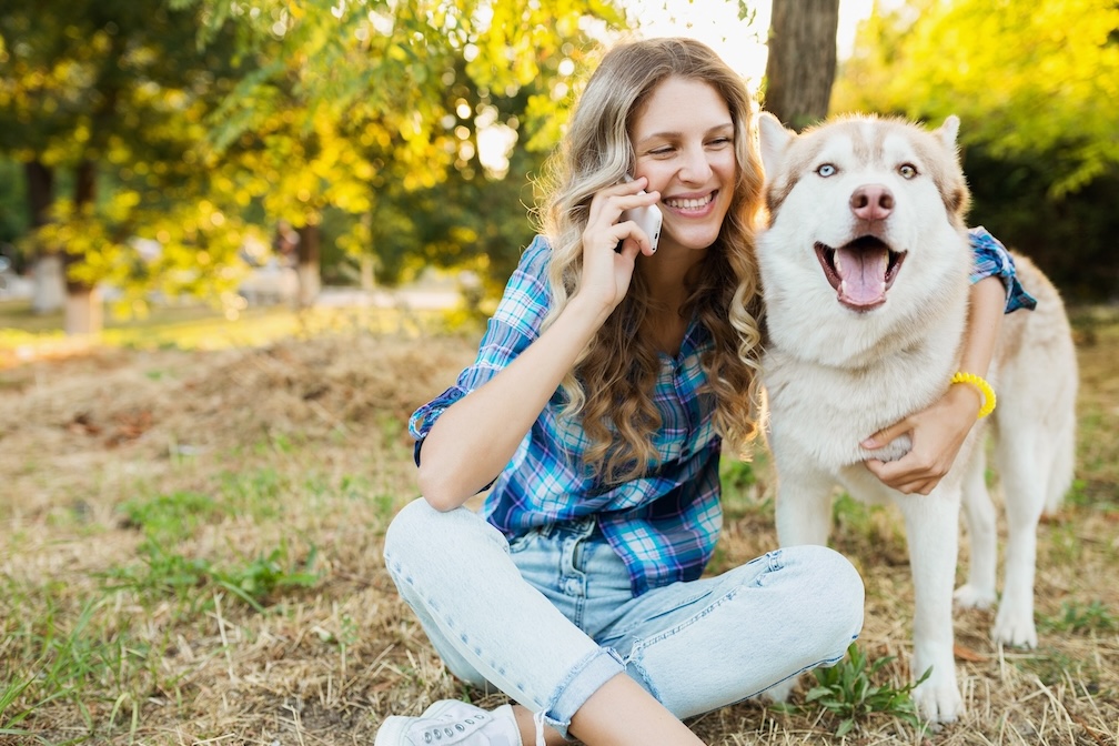 Frau telefoniert auf einer Wiese mit einem Hund im Arm