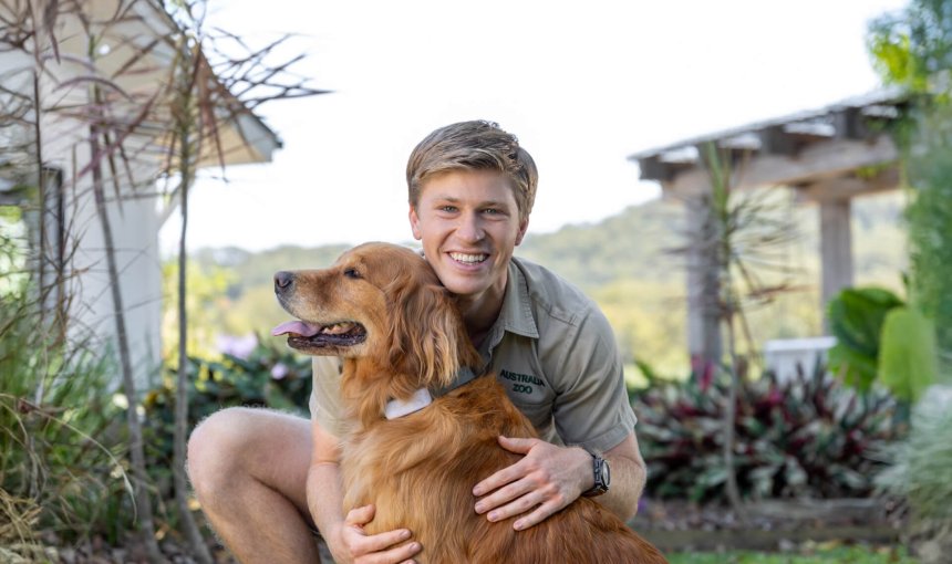 Robert Irwin cuddling a dog with a Tractive tracker in a garden